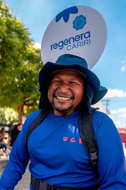 Agente de limpeza sorrindo, com a placa da campanha na cabeça